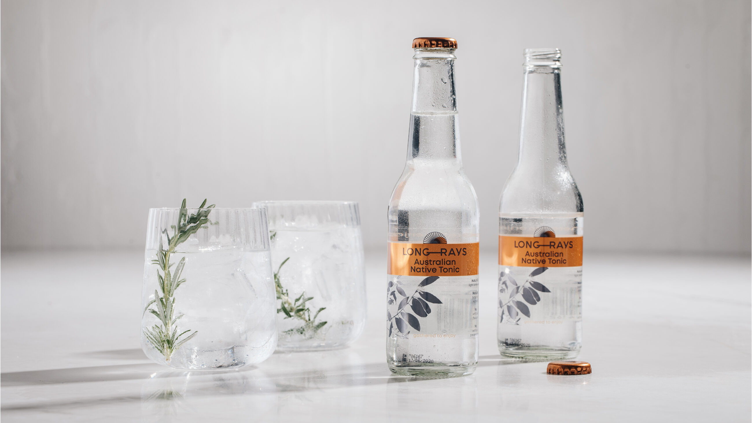 Two glasses next to two bottles of Long Rays Native Tonic with symbolic brand icon.