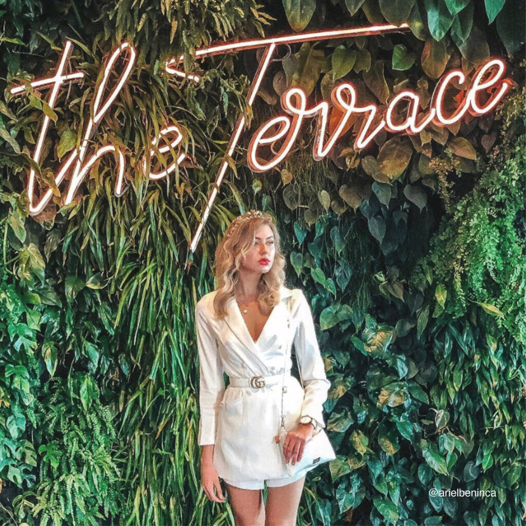 The Terrace- new sub-brand. Photo of a girl in front of neon sign and plant wall