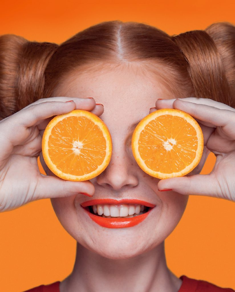 Woman holding sliced oranges in front of her eyes